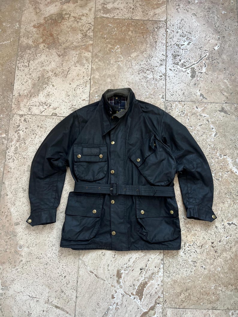 Peut inclure: Une veste en coton cir&eacute; noir avec une ceinture, plusieurs poches et des boutons en laiton.