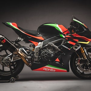 May include: A black and orange Aprilia motorcycle with green and white accents. The motorcycle has a black exhaust pipe and a black seat.