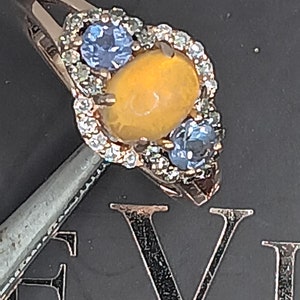May include: A gold ring with a large yellow gemstone surrounded by smaller white gemstones. Two smaller blue gemstones are on either side of the yellow gemstone.