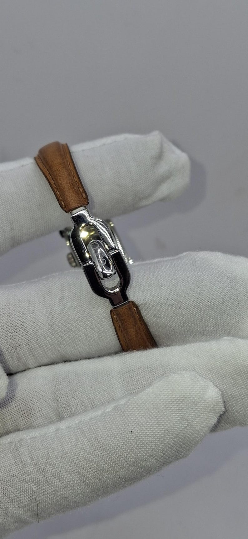 May include: A silver-toned watch with a brown leather strap. The watch has a rectangular face and a sleek, modern design. The strap is made of genuine leather.