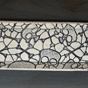 May include: Oval ceramic serving tray with a cream-colored base and a black, intricate, web-like pattern. The design includes skull and crossbones motifs, creating a unique and decorative piece. The tray is ideal for serving appetizers or displaying small items.
