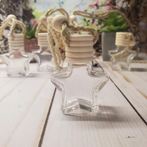 May include: A collection of clear glass star-shaped bottles, each featuring a light-colored wooden cap and a thick, braided beige hanging cord with subtle gold metallic threading, designed for holding small amounts of liquid or fragrance.