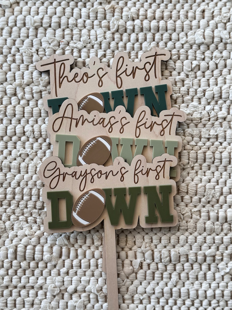 May include: Three wooden signs with the words "Theo's first down", "Amias's first down", and "Grayson's first down" with a football graphic on each sign.