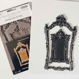 May include: A black, ornate frame mold with a rectangular center, displayed on a white surface. The mold is a vintage reflection design. A package of Décor Moulds is visible, with the text "Vintage Reflection". The mold measures 5 x 8 inches.