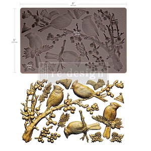 Puede incluir: Un molde de silicona marrón de 20,3 cm por 12,7 cm con diseños en relieve de cardenales en ramas, bayas y gorros pequeños. Debajo, un vaciado de color dorado muestra los resultados detallados del molde, incluyendo aves y piñas de pino.