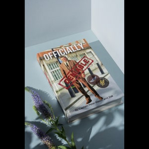 Könnte beinhalten: Ein Buch mit dem Titel "Offiziell dementiert" von Captain Peter Mason und Zoe. Das Cover zeigt einen Mann im Anzug, der vor einem Gebäude steht, über dem ein roter Stempel mit der Aufschrift "Dementiert" angebracht ist.