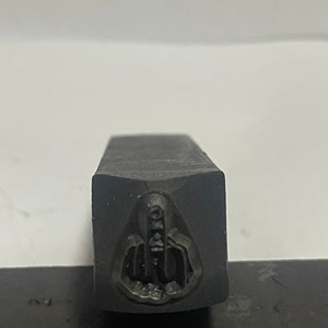 May include: A black metal stamp with a raised middle finger design.