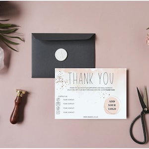 May include: A rectangular thank you card with a watercolor wash, gold foil accents, and the text THANK YOU. The card includes placeholders for contact information and a logo. A black envelope with a white wax seal, a stamp, and scissors are present.