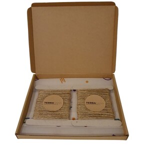 May include: Two rolls of natural twine are packaged in a cardboard box. The twine is wrapped around a cardboard circle with the text "TERRASANA" printed on it.
