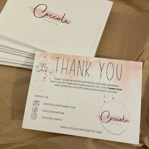 May include: A stack of white rectangular thank you cards featuring a soft pink watercolor wash and gold speckle accents. The text reads THANK YOU, includes a discount code, contact email, social media handles, and the website CoccoleCraftsUK.Etsy.com.