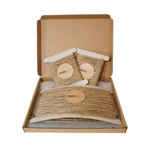 May include: A brown cardboard box containing three rolls of natural twine. The twine is wrapped in paper with a brown label that reads "TERRA-SANA".