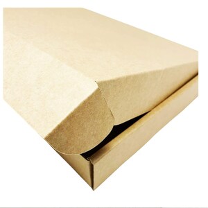 May include: A rectangular shipping box made of light brown cardboard. The box features a hinged lid with a fold-over flap design that tucks into the front edge. The surface has a matte, textured finish consistent with standard corrugated paper material.