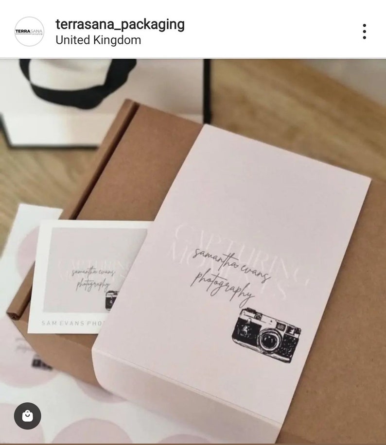 May include: A brown cardboard shipping box wrapped with a pale pink paper band featuring the text "CAPTURING MOMENTS" and "samantha evans photography" in a script font, accompanied by a small matching card with the same camera illustration.
