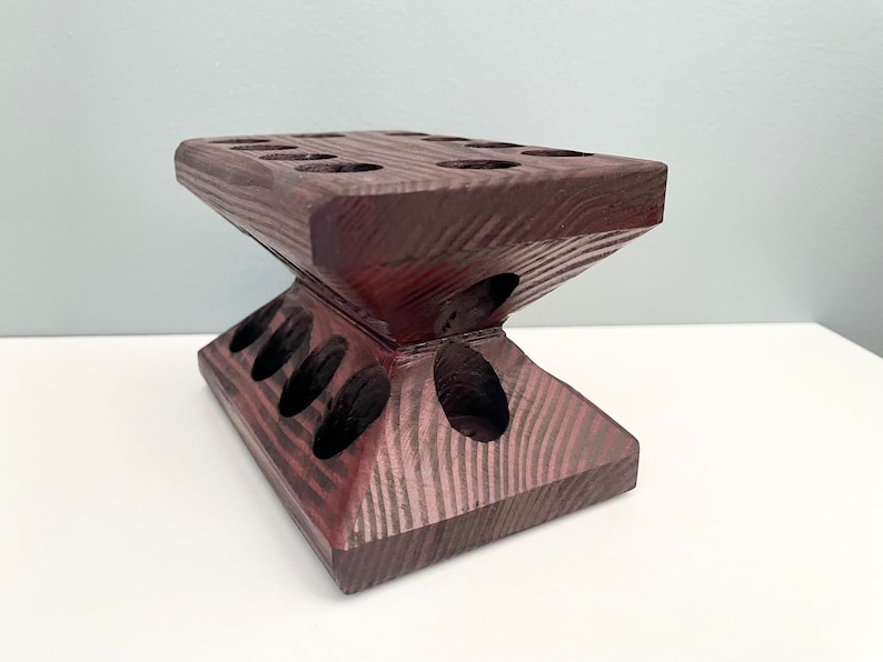 Puede incluir: Un soporte de madera marr&oacute;n oscuro con m&uacute;ltiples agujeros para sostener objetos. El soporte tiene forma de pir&aacute;mide con una parte superior plana.