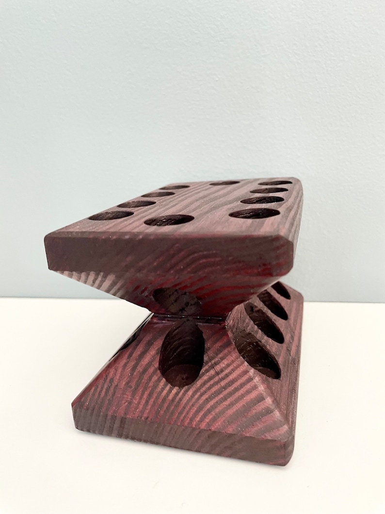 Puede incluir: Un soporte de madera con m&uacute;ltiples agujeros para sostener objetos, como pinceles o l&aacute;pices. El soporte est&aacute; hecho de madera oscura con un tono marr&oacute;n rojizo y tiene un dise&ntilde;o &uacute;nico y angulado.