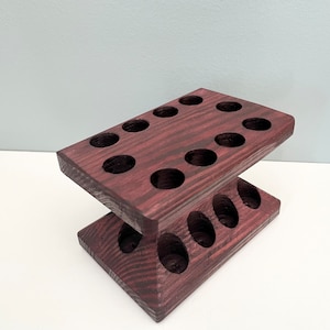 Puede incluir: Un soporte de madera de dos niveles con 13 agujeros redondos, te&ntilde;ido de un color morado oscuro. El soporte est&aacute; dise&ntilde;ado para contener objetos peque&ntilde;os como aceites esenciales u otros l&iacute;quidos.
