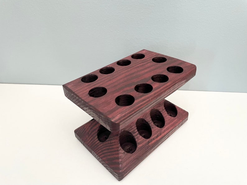 Puede incluir: Un soporte de madera de dos niveles con 13 agujeros redondos, te&ntilde;ido de un color morado oscuro. El soporte est&aacute; dise&ntilde;ado para contener objetos peque&ntilde;os como aceites esenciales u otros l&iacute;quidos.