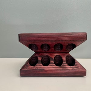 Puede incluir: Un soporte de madera de color morado oscuro con ocho recortes ovalados. El soporte tiene forma de V, con la parte superior de la V recortada para crear una superficie plana.