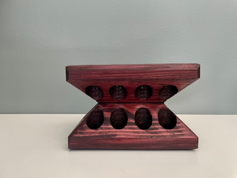 Puede incluir: Un soporte de madera de color morado oscuro con ocho recortes ovalados. El soporte tiene forma de V, con la parte superior de la V recortada para crear una superficie plana.