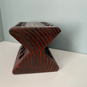 May include: A dark brown wooden stand with multiple slots for holding items, such as pencils or paintbrushes. The stand is shaped like a V and has a smooth, polished finish.