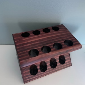 May include: A dark brown wooden stand with multiple circular cutouts, designed to hold items like toothbrushes or makeup brushes.