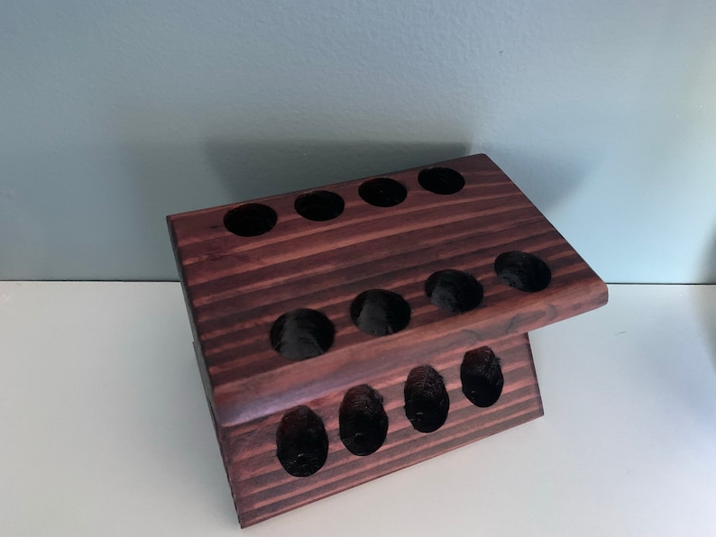 May include: A dark brown wooden stand with multiple circular cutouts, designed to hold items like toothbrushes or makeup brushes.