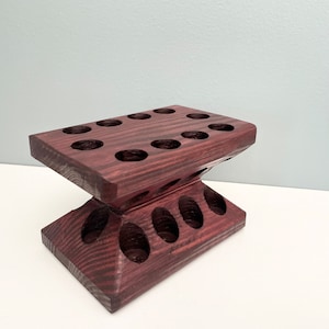 Puede incluir: Un soporte de madera oscura con m&uacute;ltiples agujeros redondos para sostener objetos. El soporte est&aacute; hecho de madera oscura con una textura granulada.