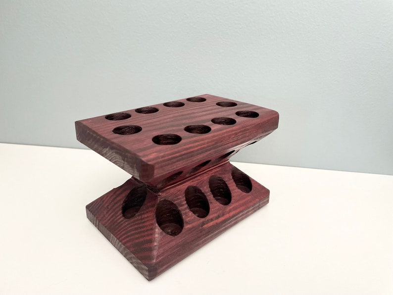 Puede incluir: Un soporte de madera oscura con m&uacute;ltiples agujeros redondos para sostener objetos. El soporte est&aacute; hecho de madera oscura con una textura granulada.