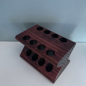May include: A dark brown wooden stand with 12 round holes, designed to hold small items like essential oils or paint tubes.