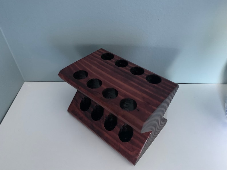 May include: A dark brown wooden stand with 12 round holes, designed to hold small items like essential oils or paint tubes.