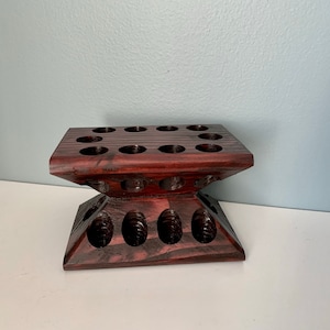 Puede incluir: Un soporte de madera oscura con m&uacute;ltiples agujeros circulares, dise&ntilde;ado para contener objetos peque&ntilde;os como aceites esenciales u otras botellas.