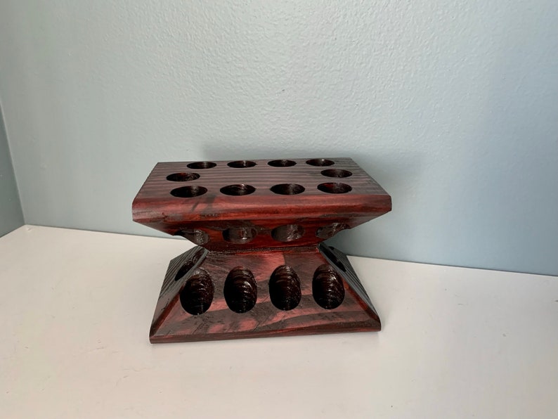 Puede incluir: Un soporte de madera oscura con m&uacute;ltiples agujeros circulares, dise&ntilde;ado para contener objetos peque&ntilde;os como aceites esenciales u otras botellas.