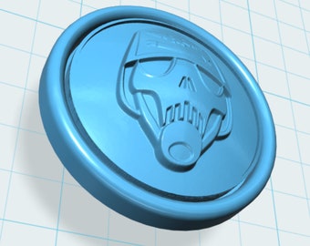 Op de afbeelding: Een lichtblauw, cirkelvormig embleem met een verhoogd ontwerp van een schedelachtig gezicht. Het embleem heeft een verhoogde rand en een gedetailleerd, driedimensionaal uiterlijk. Het ontwerp is gecentreerd op het embleem.