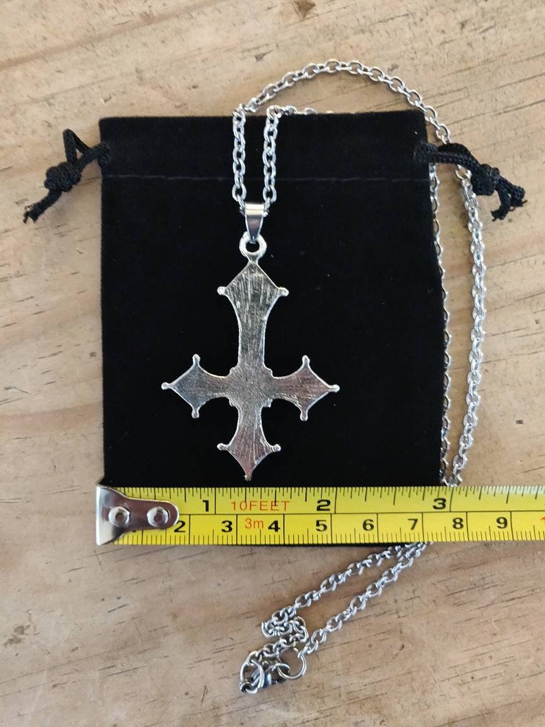 Pode incluir: Um colar com um pingente de prata em forma de cruz adornada. O colar mede 5 cm de comprimento e vem com uma bolsa de veludo preto.
