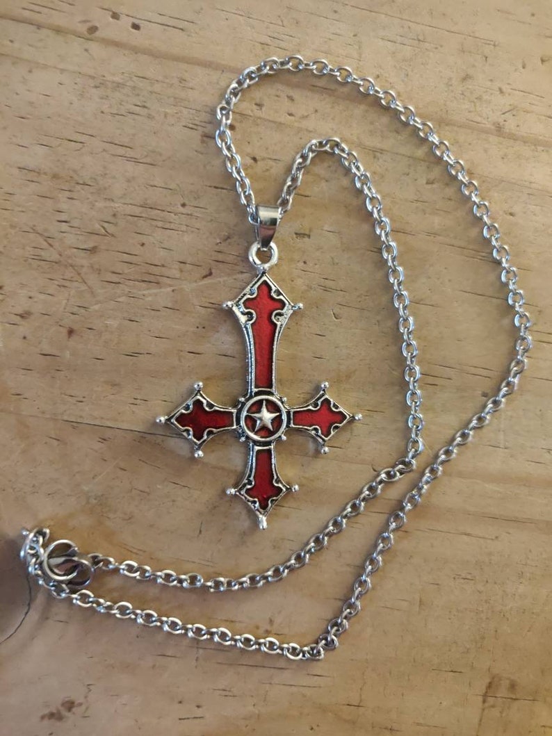 Pode incluir: Um colar de corrente de prata com um pingente de cruz vermelha e prateada. A cruz tem uma estrela de cinco pontas no centro.