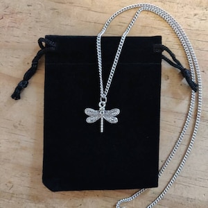 May include: A silver chain necklace with a dragonfly pendant. The necklace is in a black velvet pouch.