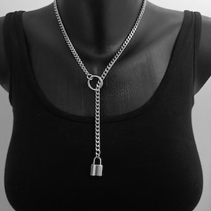 May include: A silver chain necklace with a small padlock pendant. The necklace has a curb chain design and a circular ring detail. The pendant hangs from a vertical chain, creating a Y-shape. The necklace is displayed on a black mannequin.