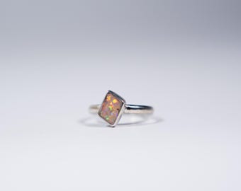 May include: A silver ring with a rectangular opal gemstone. The opal is a light pink color with iridescent flashes of green and blue.