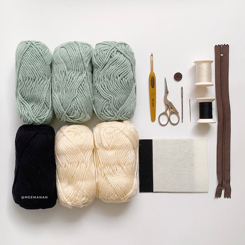 May include: A craft supply kit for crocheting a project. The kit includes six balls of yarn in green, white, and black, a crochet hook, a pair of scissors, two needles, a zipper, and two spools of thread.
