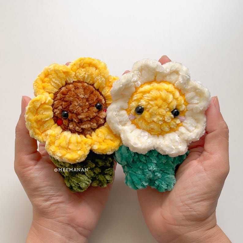 Pu&ograve; includere: Due peluche di fiori fatti a mano all'uncinetto. Uno &egrave; un girasole con petali gialli e un centro marrone. L'altro &egrave; una margherita con petali bianchi e un centro giallo. Entrambi hanno occhi neri e steli verdi.