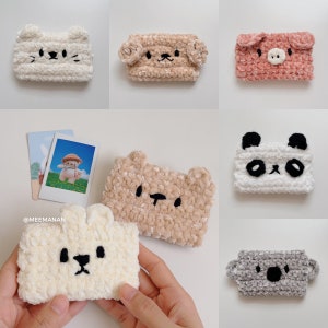 K&ouml;nnte beinhalten: Eine Sammlung handgefertigter, pl&uuml;schtierf&ouml;rmiger Kartenhalter. Die Designs umfassen eine Katze, einen Hund, ein Schwein, einen B&auml;ren, einen Panda, einen Koala und ein Kaninchen. Jeder Kartenhalter ist aus weichem, strukturiertem Garn gefertigt und hat gestickte Gesichtsdetails.