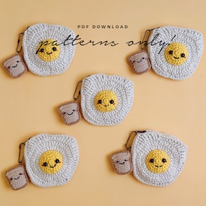May include: Five crocheted amigurumi toys, including four egg-shaped coin purses with smiling faces and one toast-shaped keychain. The egg-shaped purses are beige with yellow yolks and black eyes. The toast keychain is brown with a smiling face. The text "PDF DOWNLOAD patterns only!" is printed on a white background.
