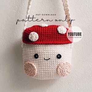 May include: Crochet pattern for a mushroom-shaped bag with a white body, red top, and white polka dots. The bag has a smiling face with black eyes and a black stitched mouth. The pattern is available as a PDF download and includes a YouTube video tutorial.