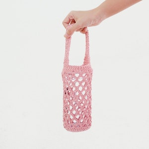Peut inclure: Un sac en crochet rose avec une anse, con&ccedil;u pour contenir une bouteille d'eau ou une autre boisson.