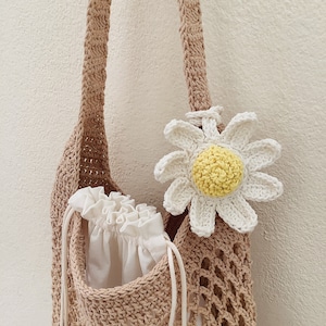 Peut inclure: Un sac cabas en crochet marron avec une fleur de marguerite en crochet blanc attach&eacute;e &agrave; la bandouli&egrave;re. Le sac est doubl&eacute; d'une doublure blanche &agrave; cordon et d'une bandouli&egrave;re en crochet blanc.