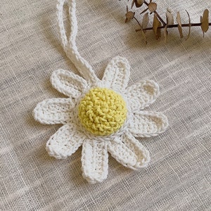Peut inclure: Une marguerite blanche en crochet avec un centre jaune. La marguerite est attach&eacute;e &agrave; un cordon blanc.