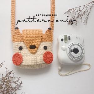 May include: Crochet pattern for a fox-shaped camera bag. The bag is made with beige, orange, and brown yarn. The pattern is available as a PDF download. "PDF Download pattern only" is written in black text on a white background.