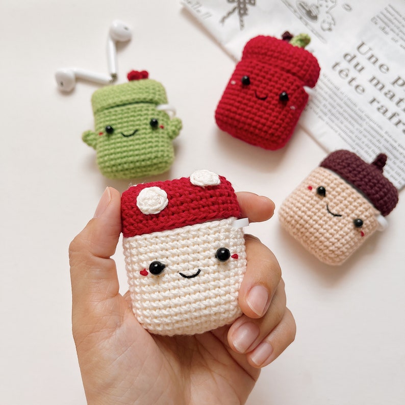May include: Four crocheted AirPod cases in the shapes of a mushroom, a cactus, an acorn, and a red pepper. Each case has a cute, embroidered face.
