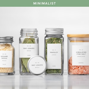 May include: A collection of glass jars with metal lids and labels, containing various spices and herbs. The jars include sesame seeds, bay leaves, parsley, and Himalayan pink salt. The word "MINIMALIST" is at the top.