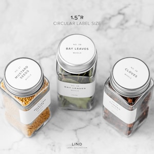 May include: Three clear glass jars with silver lids, each containing different spices: mustard seeds, bay leaves, and cloves. Each jar has a white label with black text. The text "1.5"R CIRCULAR LABEL SIZE" is at the top.